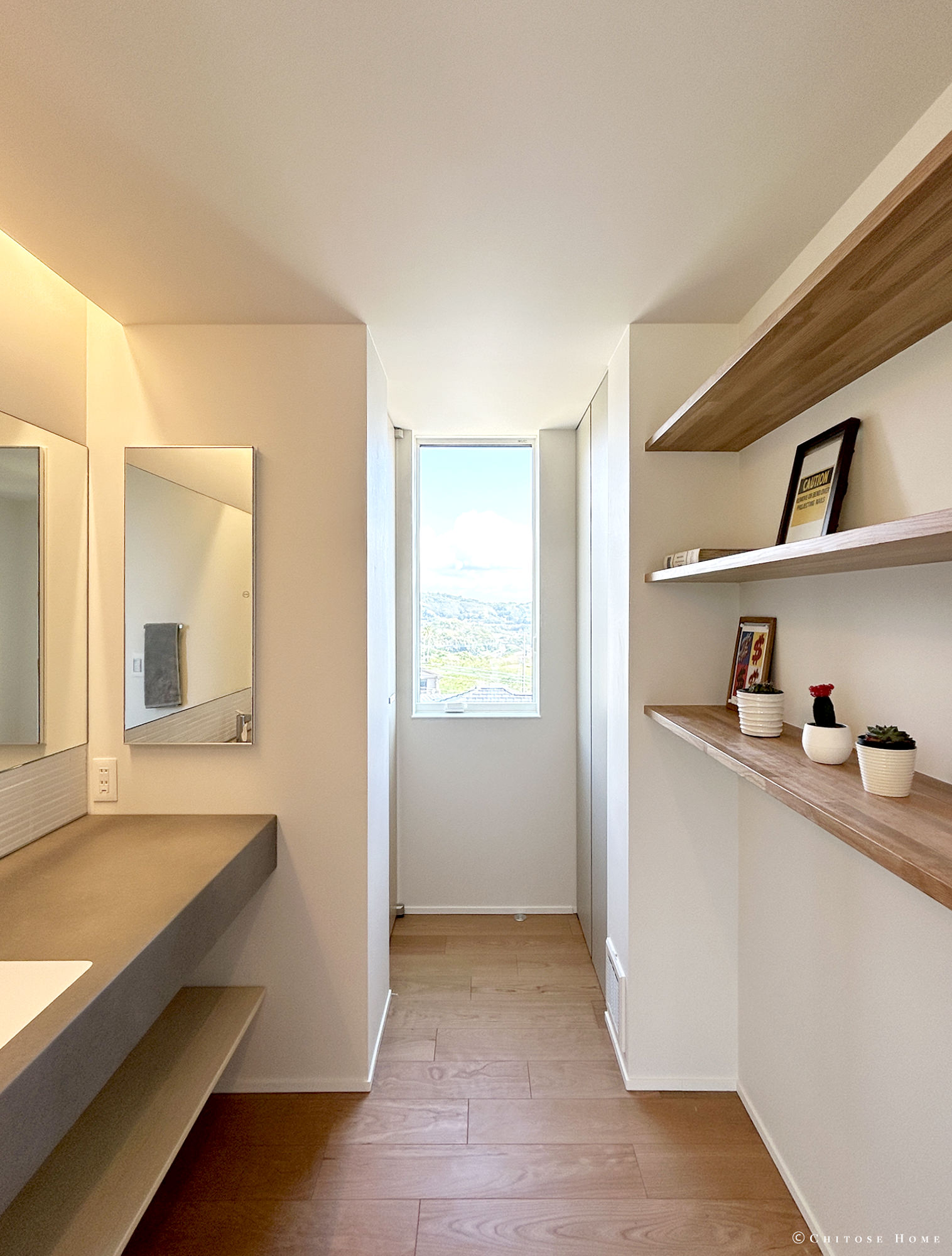洗面スペースからトイレへと繋がる動線にある廊下。突き当りの壁に天井と高さを合わせた窓を設え、抜け感を演出。無垢材を使ったシンプルな構成の棚や間接照明、壁埋め込みの鏡付き収納など、使いやすさとデザインの両立を図る。